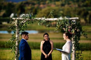 Bride and groom exchange vows under a rustic birch arch decorated with greenery and flowers.