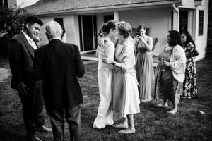 Black and white photo of wedding guests mingling and embracing outside a home.