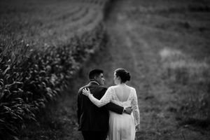 Black and white photo of bride and groom walking arm in arm through a field.