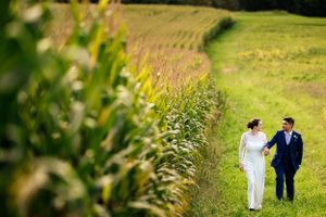 Bride and groom holding hands and walking along a green field on their wedding day.