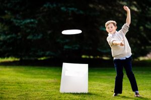 Young boy tossing a frisbee on a green lawn at an outdoor wedding reception.