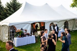 Guests mingle outside a white wedding reception tent on a lush green lawn at dusk.