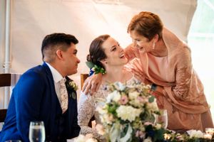 Bride and groom share a joyful moment with an older woman at the wedding reception table.