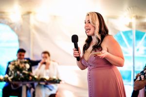 Woman in pink dress gives an emotional wedding toast speech holding a microphone.