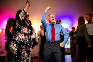 Guests dancing energetically at a wedding reception with colorful pink and purple lights.