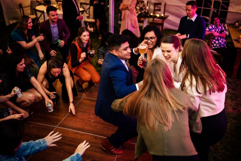 Wedding guests celebrating on dance floor with drinks during lively reception party.