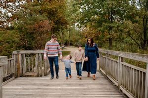Family walking together on a wooden boardwalk through autumn trees in a nature park.