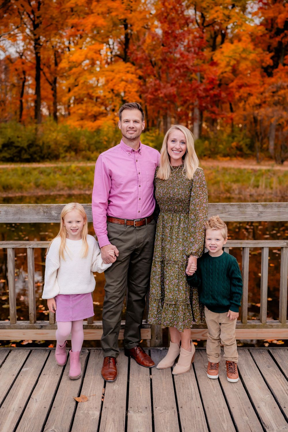 A family of four poses on a wooden deck surrounded by vibrant fall foliage.
