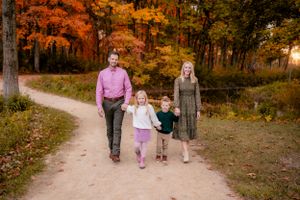 A family walks together on a winding path through colorful autumn woods.