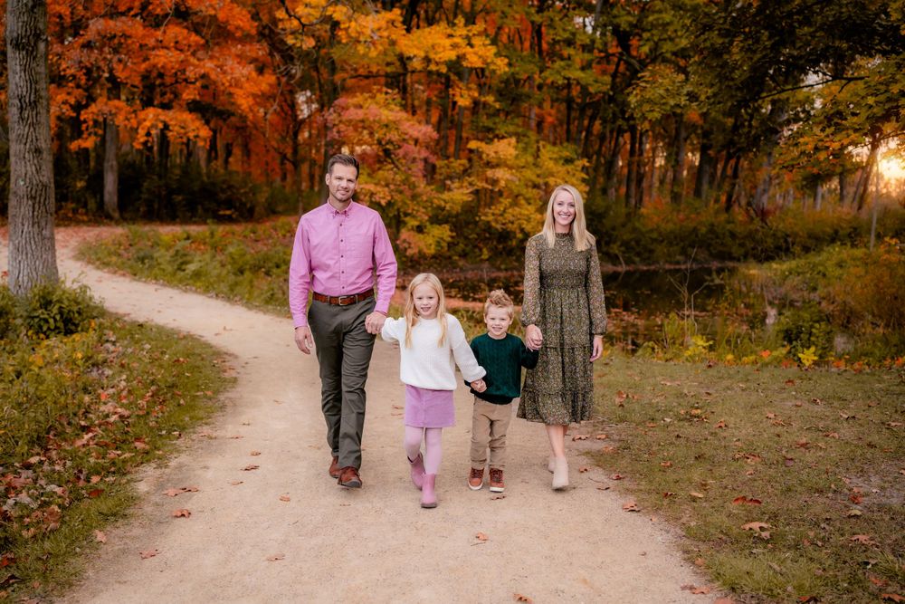 A family walks together on a winding path through colorful autumn woods.