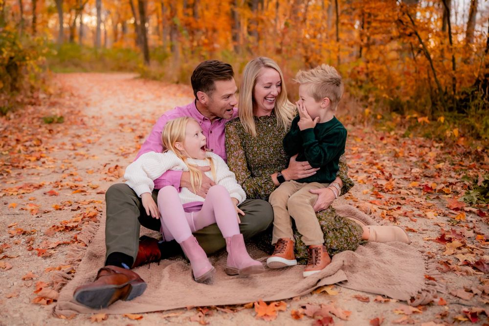 A family sits together on fallen autumn leaves in a forest path during golden hour.