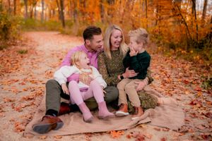 A family sits together on fallen autumn leaves in a forest path during golden hour.