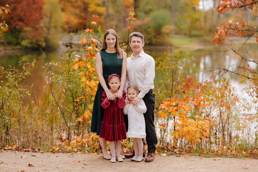Family group portrait in autumn setting with colorful fall foliage and lake in background.
