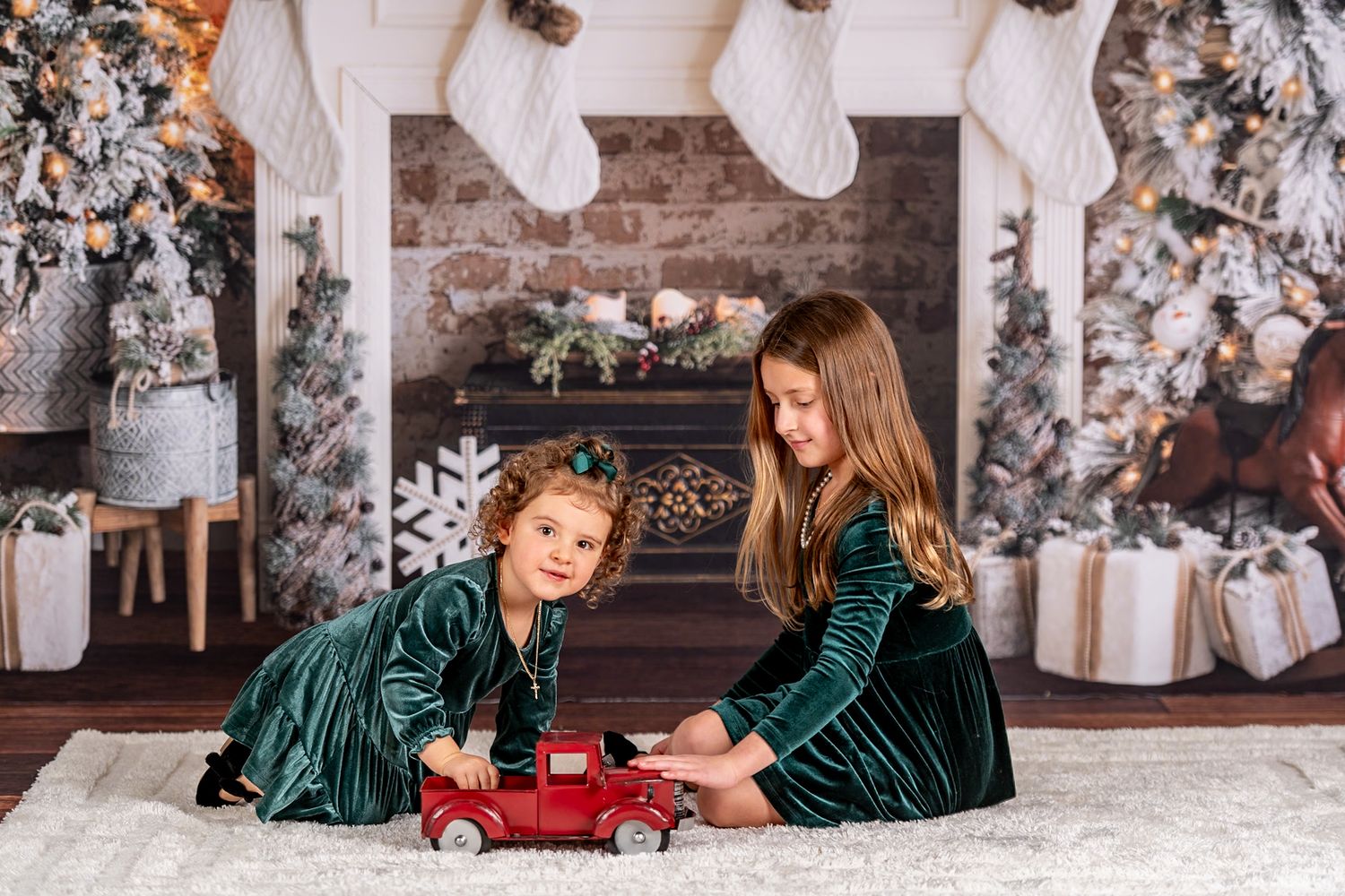 Children playing with toy car in front of decorated Christmas fireplace.