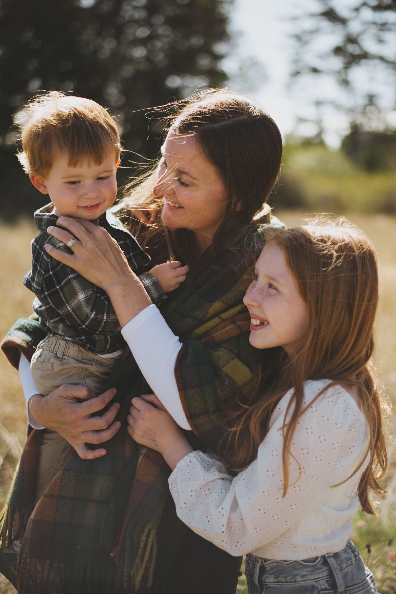A heartwarming family moment outdoors with sunlight filtering through trees in the background.