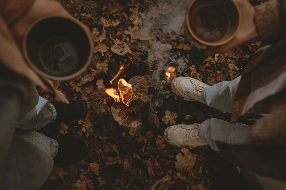 Feet gathered around campfire with fallen leaves on ground.