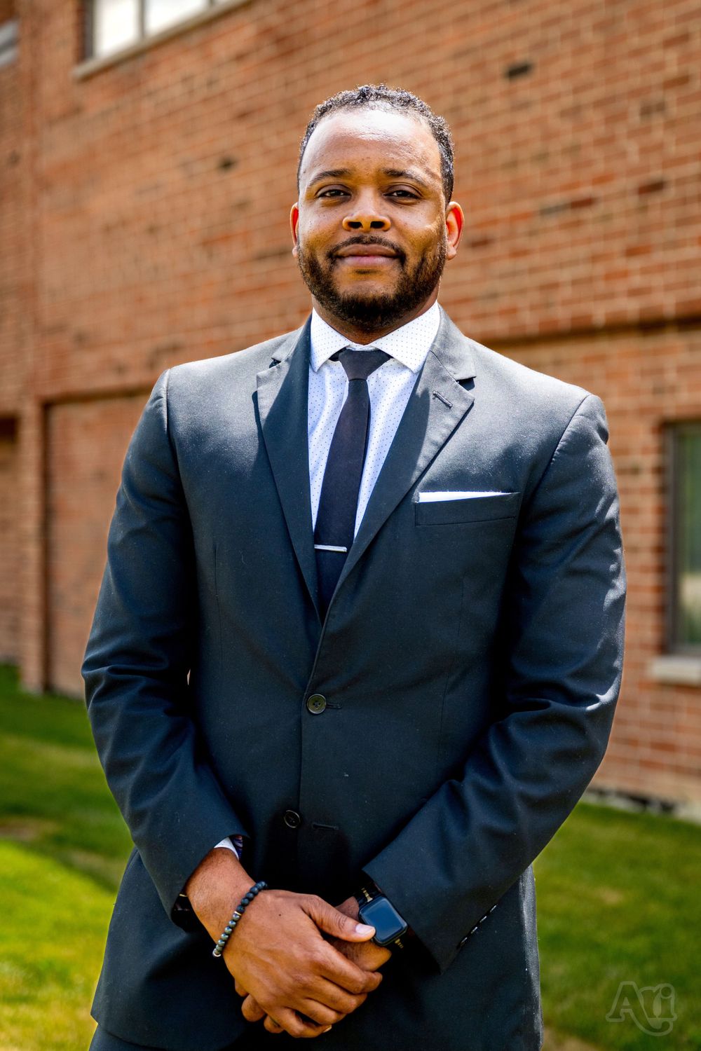 Professional portrait of person in navy suit against brick wall.