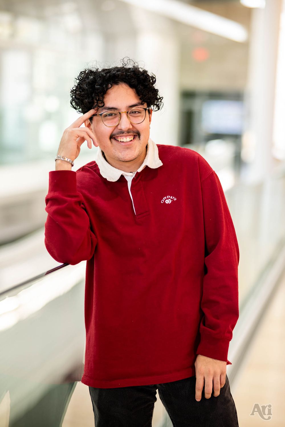 A portrait of someone in glasses and a red sweater standing by a window in a bright indoor setting.