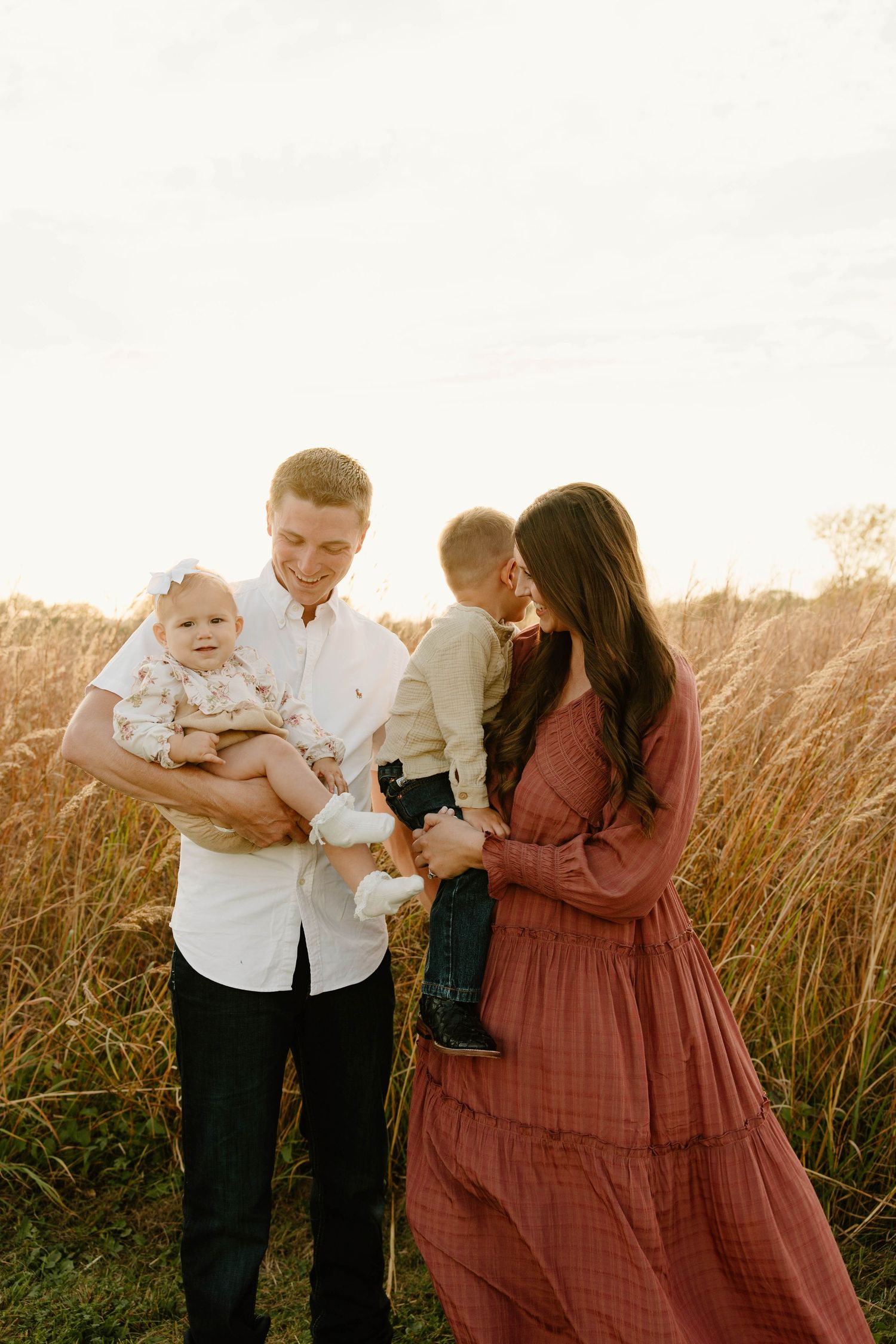 Family of four shares tender moment together in tall grass field during sunset.