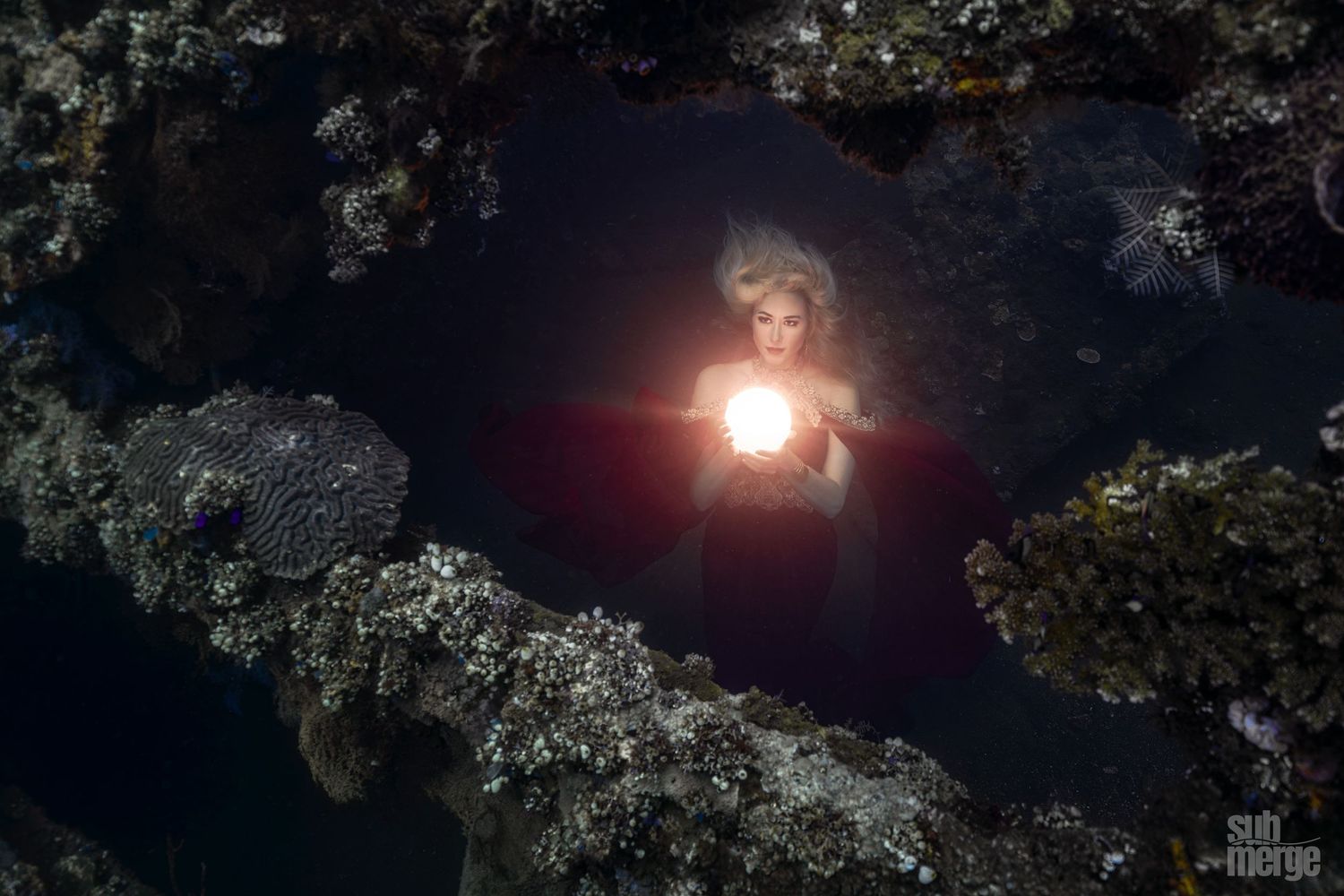 A figure in a flowing white dress poses gracefully against a dark rocky backdrop near water.