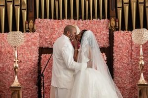 Wedding couple poses against a pink floral backdrop with gold candelabras in an elegant setting.