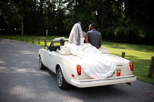 White vintage convertible wedding car with flowing fabric decorations parked in a lush garden setting.