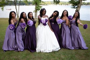 Wedding party in purple bridesmaid dresses poses on grass near a lake.