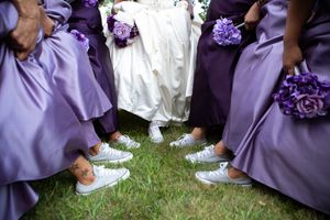Wedding party members in purple dresses seated on grass during an outdoor celebration.