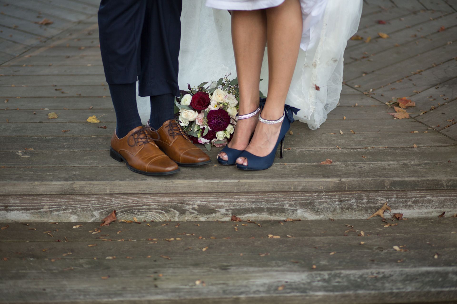Wedding party members stand together showing their shoes on a rustic wooden deck.