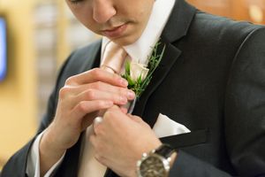 Close-up details of a groom's hands adjusting his formal black tie and white dress shirt.