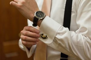 Close-up shot of formal dress watch being adjusted on wrist with white shirt sleeve.