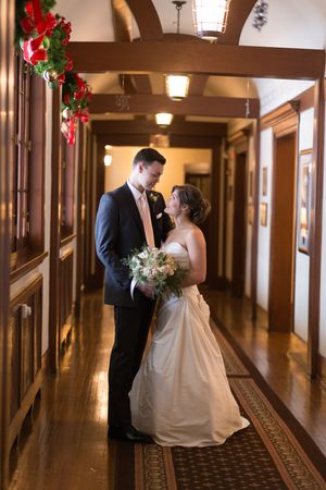 A romantic wedding couple shares intimate moments in an elegant wood-paneled hallway decorated with holiday garland.