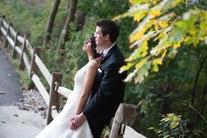 A wedding couple shares a tender moment on a rustic path surrounded by autumn foliage.
