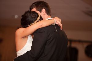 A couple embraces in a tender moment during their wedding celebration on a warm-lit dance floor.