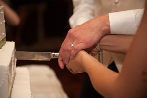 Close-up of hands cutting into a white tiered wedding cake during the reception celebration.