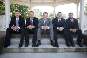 Groomsmen in dark suits sitting casually on white gazebo steps showing just their legs and shoes.