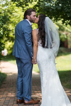 Newlywed couple shares romantic kisses in a garden setting with brick pathway and lush greenery.