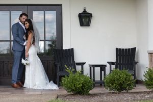 A romantic couple shares an intimate moment on a porch with white columns and black rocking chairs.