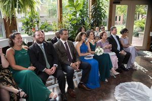 Wedding reception guests seated at tables in an elegant indoor venue with tropical plants.
