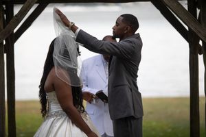 A couple shares an intimate moment under a wooden arch during their outdoor wedding ceremony.