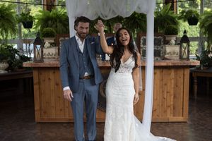 A couple in wedding attire shares a joyful moment together in a garden setting with wooden fencing.
