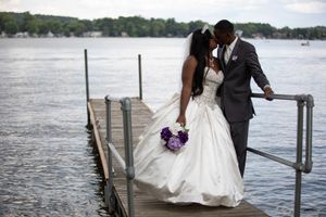 A romantic wedding couple shares an intimate moment on a dock overlooking a serene lake with purple bouquet details.
