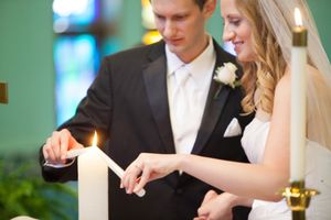 Couple lighting unity candles during an indoor wedding ceremony.