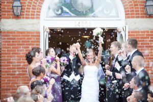 Wedding party and guests gathered outside a brick building for a celebration.