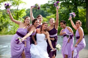 Wedding party in purple bridesmaid dresses and white gown pose together outdoors in a garden setting.