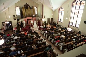Wide view of a church wedding ceremony with guests seated in wooden pews under vaulted ceilings.
