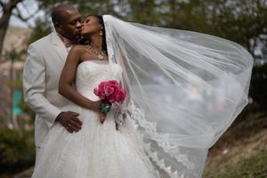 Close-up details of a flowing white wedding dress and veil against a natural outdoor backdrop.
