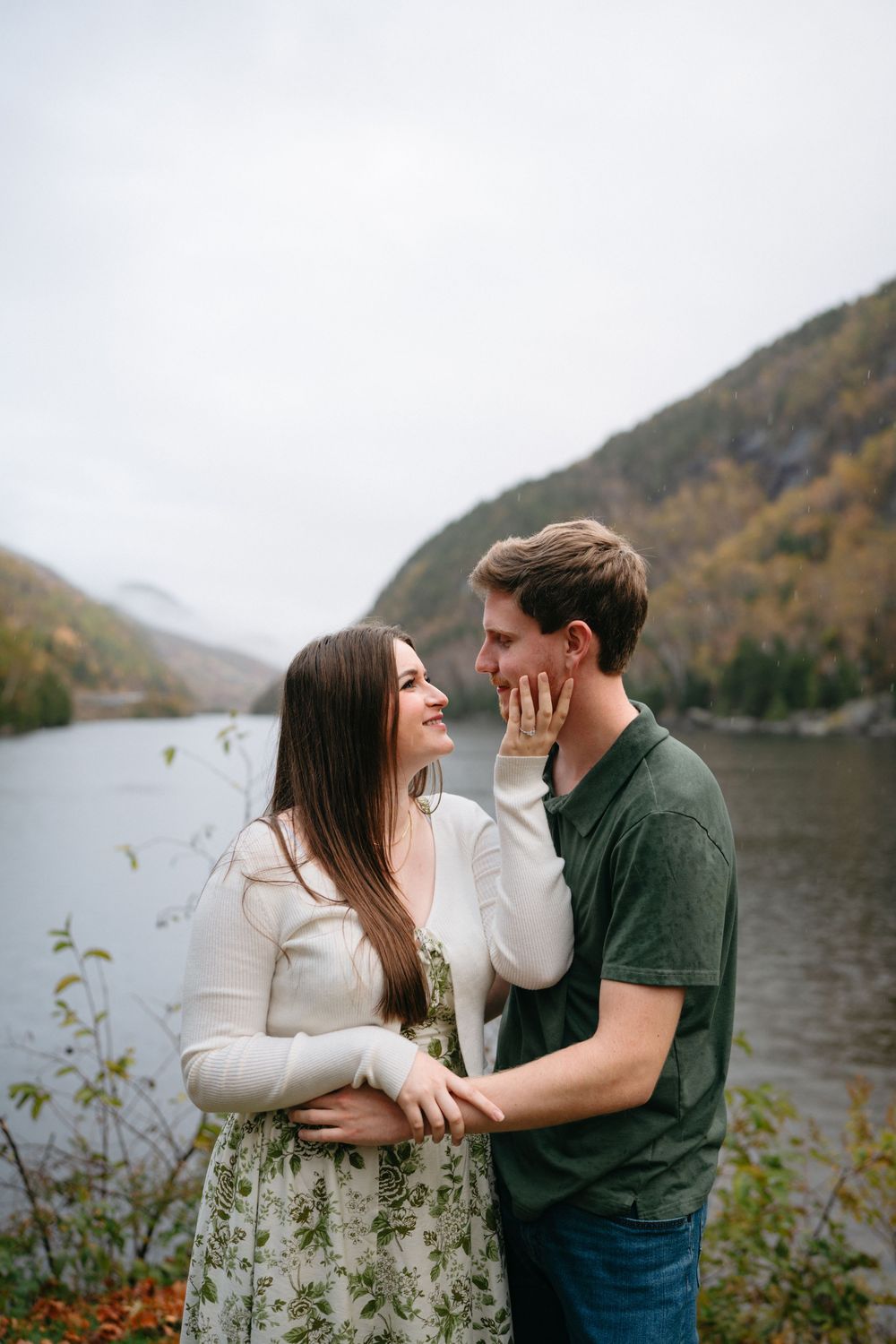 A tender moment between a couple against a backdrop of mountains and a serene lake in fall.