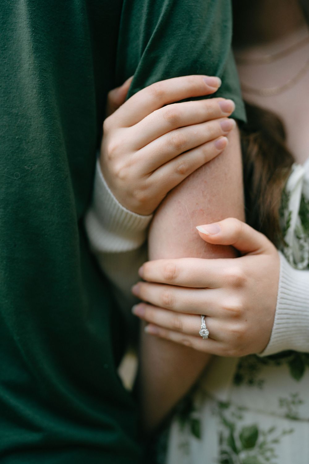 Close-up of embracing hands with an engagement ring visible against a green and white clothing background.