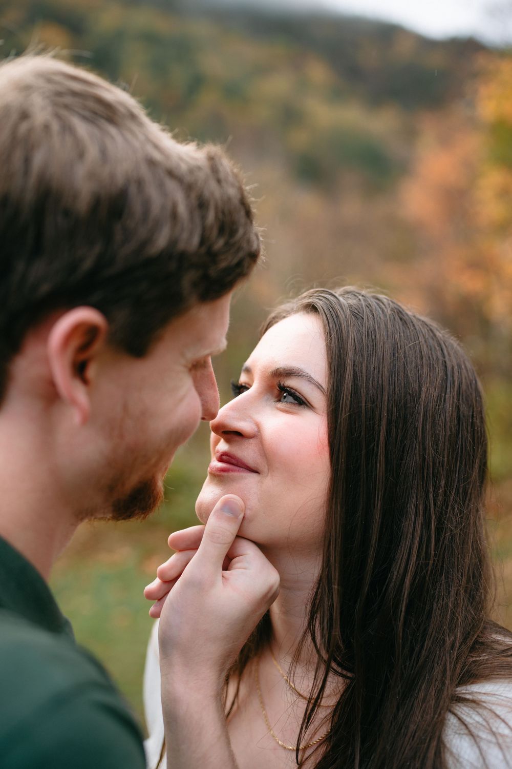 A couple shares an intimate moment outdoors during autumn with blurred nature background.
